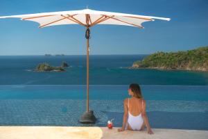 a woman sitting under an umbrella on the beach at Casa Chameleon Hotel Las Catalinas - Adults Only in Playa Flamingo