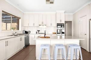 a white kitchen with white cabinets and stools at Modern home in Highton in Highton +2 photos