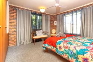a bedroom with a bed and a chair and windows at Bromeliads in Iluka