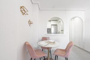 a white dining room with pink chairs and a white table at Mar y Sol in Torrevieja