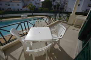a white table and chairs on a balcony with a pool at Cravinho in Albufeira