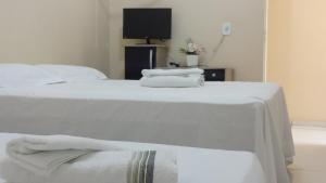 duas camas com lençóis brancos e uma televisão num quarto em Hotel Pousada Arara Azul em Barra do Garças