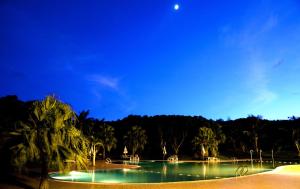 una piscina por la noche con palmeras y luna en Kentington Resort, en Manzhou