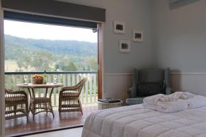 a bedroom with a bed and a balcony with a table and chairs at Greenlee Cottages in Canungra