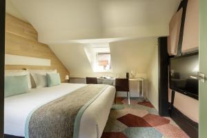a bedroom with a bed and a flat screen tv at Hotel Le Colombier Suites in Colmar