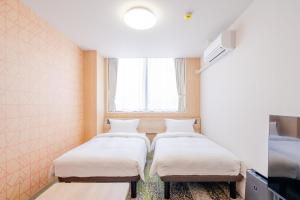 two beds in a room with a window at たびのホテル佐渡Annex in Sado