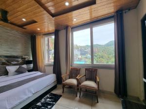 a bedroom with a bed and two chairs and a window at Hotel Rajinder Prasth in Dalhousie