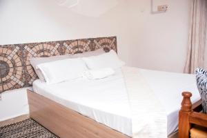 a bed with white sheets and pillows in a room at Angie's Cozy Studio Diani Beach in Ukunda