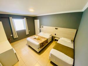 a hotel room with two beds and a window at Pousada Nosso Lar - Opte sem ou com Café, Estacionamento e a uma Quadra da Praia in Guarujá +9 photos