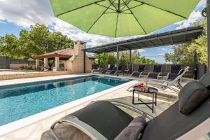 a swimming pool with a green umbrella and chairs and a table at Villa Balen ZadarVillas in Lisičići