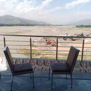 Zwei Stühle stehen auf einem Balkon und blicken auf ein Feld. in der Unterkunft River Breeze Hotel in Mingora