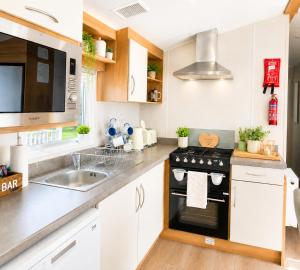 a kitchen with white cabinets and a black stove top oven at Magic Caravan Camber Sands 221 in Camber