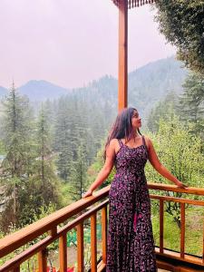 a woman in a dress standing on a balcony at Jibhi Dreams in Jibhi
