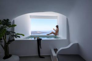 a woman sitting on a window sill in a bathroom at Dagaz Suites in Fira