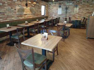 a restaurant with wooden tables and chairs and a brick wall at Pingvin Panzió in Komárom