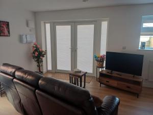 a living room with a leather couch and a flat screen tv at Ives End in Buxton