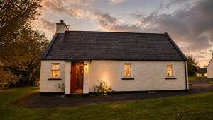 a small white house with a black roof at Wild Rowan Cottage - 2 Bedroom in Louisburgh