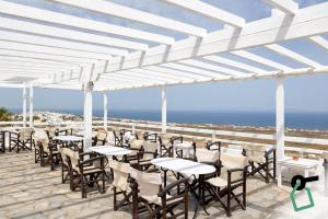 a row of tables and chairs on a patio with the ocean at Hotiday Santorini Seafront in Santorini