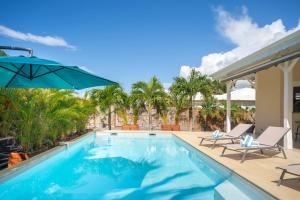a swimming pool with chairs and an umbrella at Villa Ti'Palm in Saint-François
