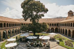 an courtyard with a tree and tables and umbrellas at Monasterio, A Belmond Hotel, Cusco in Cusco