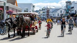 a horse drawn carriage and people riding bikes down a street at Above Mustang Condos in Mackinac Island