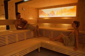 un hombre y una mujer sentados en una sauna en Alledolomiti Boutique Lake Hotel - Adults friendly, en Molveno