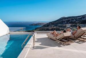 two people laying in lounge chairs next to a swimming pool at Anemolia Villas in Karpathos