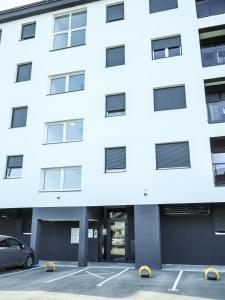 a white building with a car parked in a parking lot at Nada Apartman in Prijedor