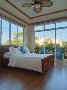 a bedroom with a bed with a ceiling fan and large windows at KRUEGERs Cottage in Sipalay