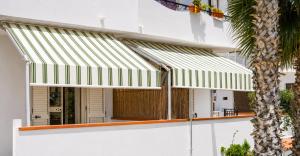 awnings on a white building with a palm tree at Appartamenti ABR Porto in Le Castella