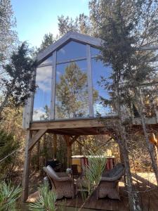 a glass house on a wooden deck with wicker chairs at Üügumetsa treehouse and sauna in Kallaste