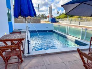 a pool with an umbrella and two chairs and a table at Flats Praia de Gravatá in São José da Coroa Grande