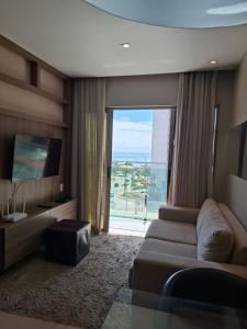 a living room with a couch and a large window at Brisa Calma Premium Flat - PontaNegra in Natal