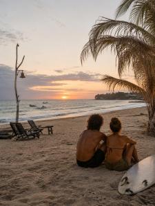 two people sitting on the beach watching the sunset at Beachfront - Private Floor, 4 Rooms - Casa 3 Lunas in Playa Agua Blanca