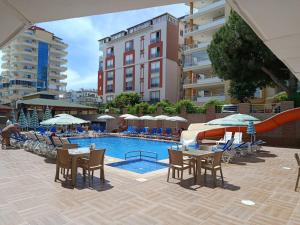 ein Schwimmbad mit Tischen und Stühlen neben einem Gebäude in der Unterkunft Bariscan Hotel in Mahmutlar