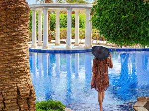 a woman wearing a hat standing next to a swimming pool at Mövenpick Resort & Residences Aqaba in Aqaba