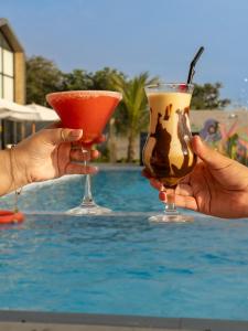 two hands holding two cocktails in front of a pool at Awqa Loft & Camp in Trujillo