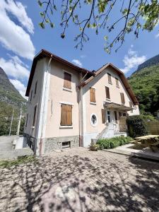 a large white building with wooden windows and mountains at L'escale de l'oisans in Livet-et-Gavet