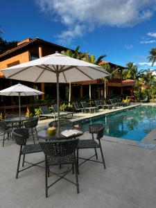 a table and chairs with an umbrella next to a pool at Vila Anambé in Uruçuca