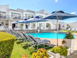 a pool with blue umbrellas and lounge chairs and a pool at Arniston Hotel Manor House in Arniston