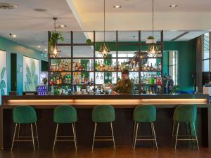 a bar with green chairs and a bartender at Novotel Melbourne Glen Waverley in Glen Waverley