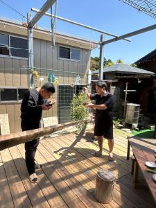 two men standing on a deck playing with a plant at ログハウス1棟貸し,持込み自由,サウナ,露天風呂にバーべキュウや薪割り,ソーメン流しに収穫体験が楽しめます in Kashima