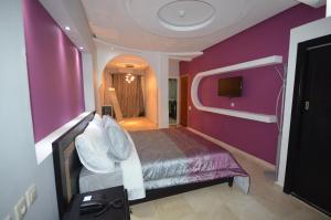 una camera da letto con parete viola, letto e TV di Hôtel-Café-Restaurant Pyramides, a Taza