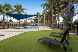 a yard with two chairs and an umbrella and a pool at Carrum Downs Motel in Carrum Downs