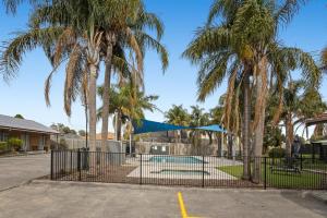 a fence with palm trees in front of a pool at Carrum Downs Motel in Carrum Downs