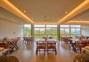 a restaurant with tables and chairs and windows at Nature Green Pool Resort Munnar by VOYE HOMES in Munnar