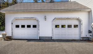 two white garage doors in a white house at Spacious Seven Peaks Ridge Quiet Side Hot Tub, Pet Friendly, Fire Pit & Deck in Southwest Harbor