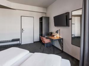 a hotel room with a bed and a desk and a tv at B&B HOTEL Rüsselsheim in Rüsselsheim