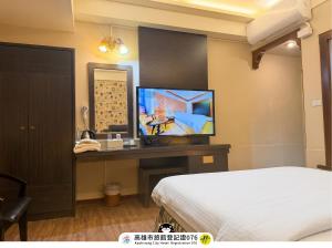 a bedroom with a bed and a desk with a television at I HI Sanduo Travel Hotel in Kaohsiung