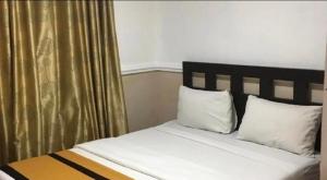 a bedroom with a bed with white pillows and gold curtains at kiwi budget hotel in Rawang
